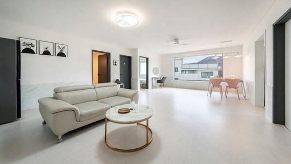 A modern living room with a sofa, a coffee table, and a dining area with chairs. There are framed pictures on the wall and a view of a building outside. - Gyeongju Purspet Dog Pension (Gyeongju)