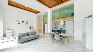 A modern living room with a grey sofa, a dining table with chairs, and a kitchen area with a fridge and stove. - Gyeongju Purspet Dog Pension (Gyeongju)