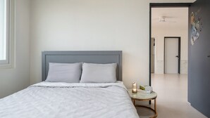 A neatly made bed with a grey headboard, a bedside table with a book and a candle, and a hallway leading to a bathroom. - Gyeongju Purspet Dog Pension (Gyeongju)
