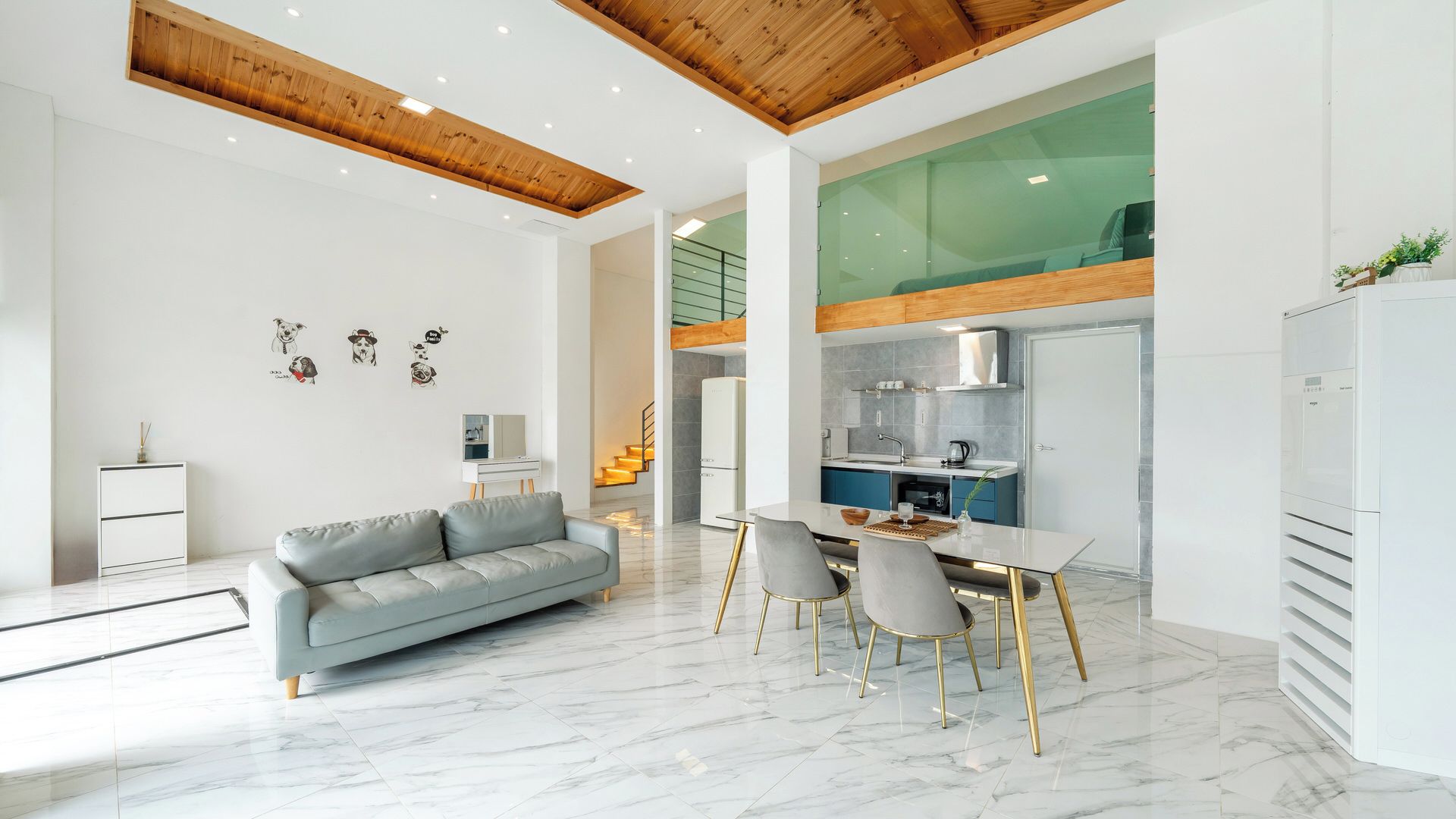 A modern living room with a grey sofa, a dining table with chairs, and a kitchen area with a refrigerator and stove.