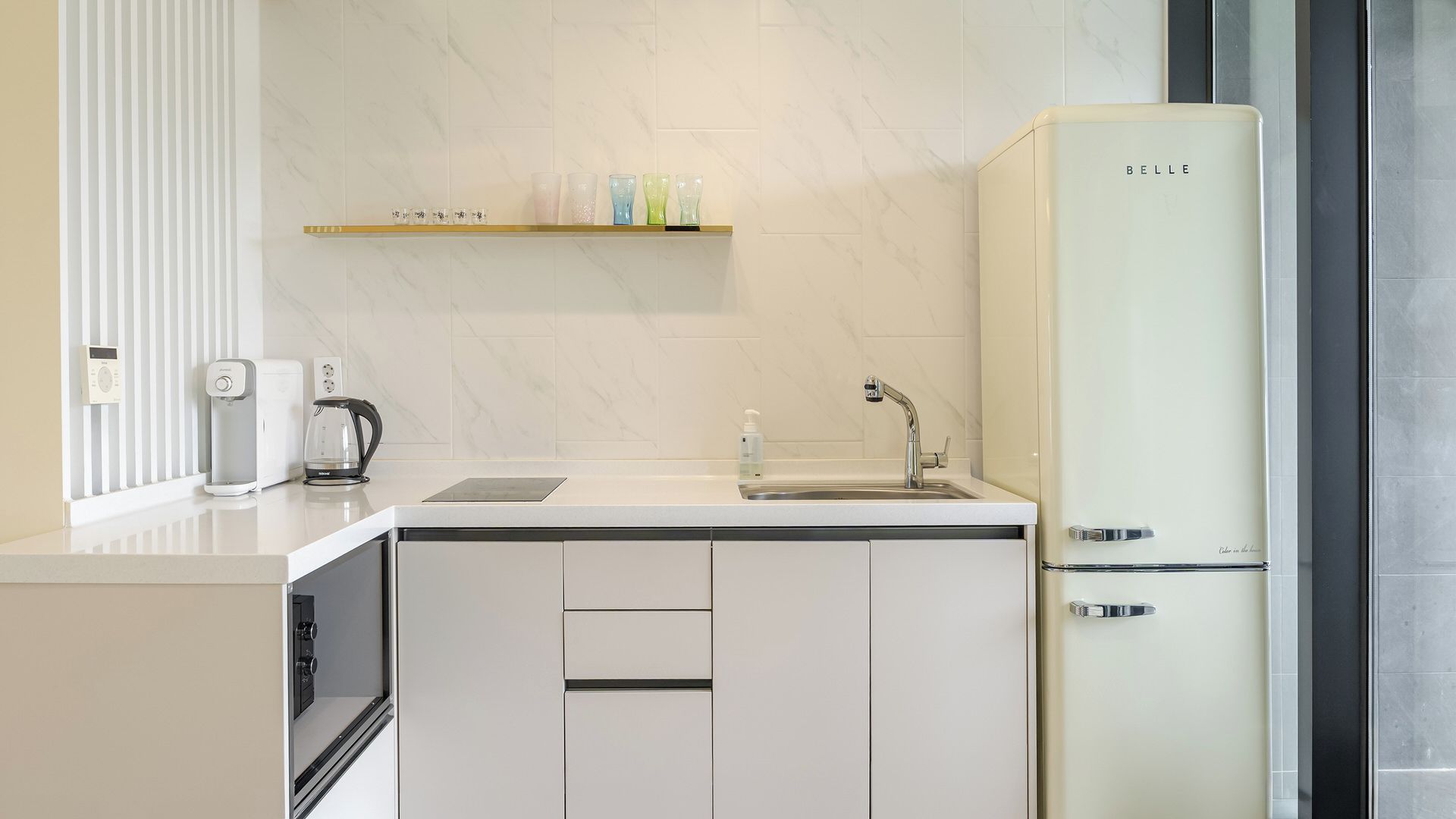 A modern kitchen with a built-in refrigerator, a coffee maker, and a shelf with glassware.