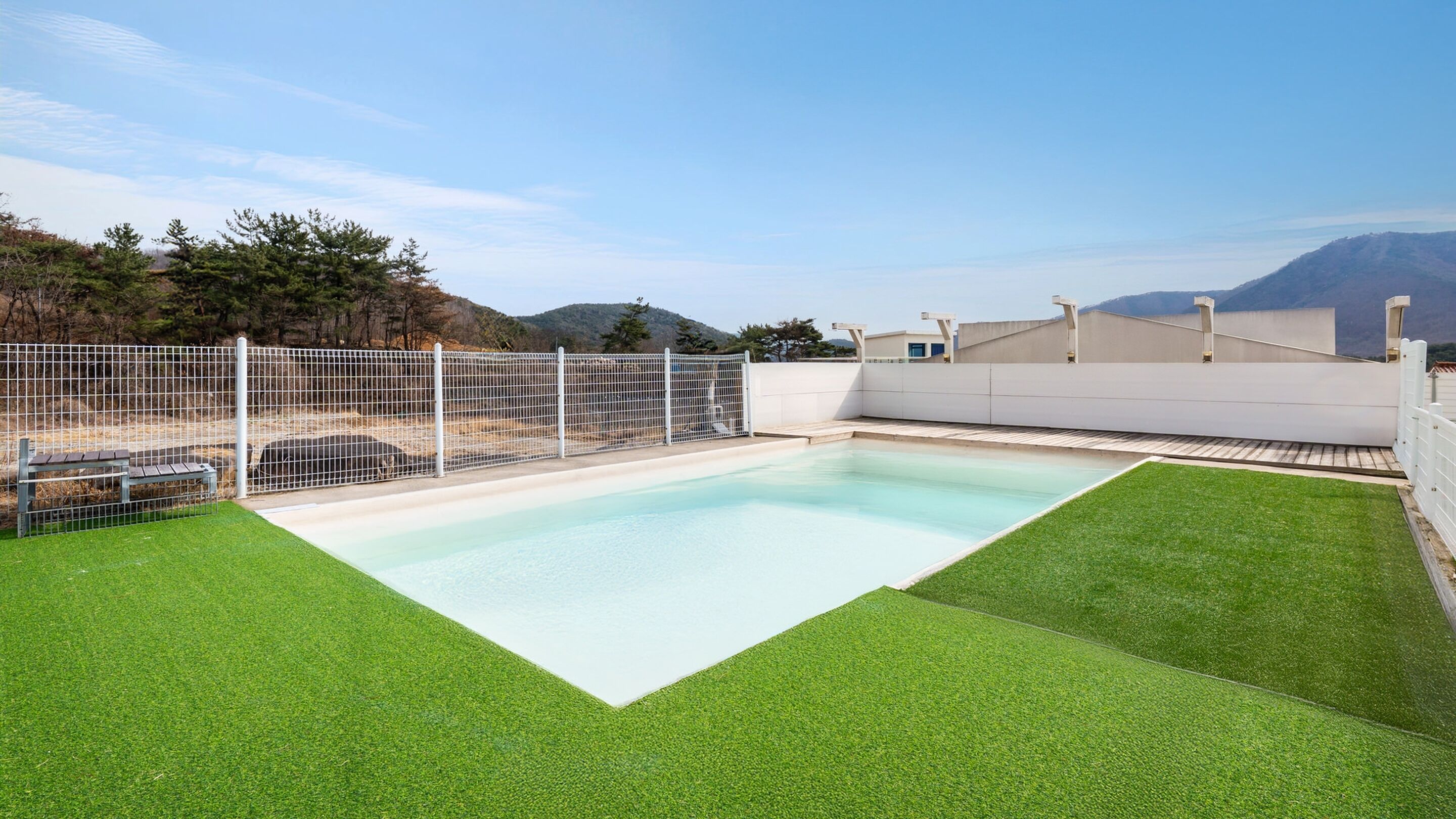 Una piscina rectangular con cerca blanca y césped artificial a su alrededor.