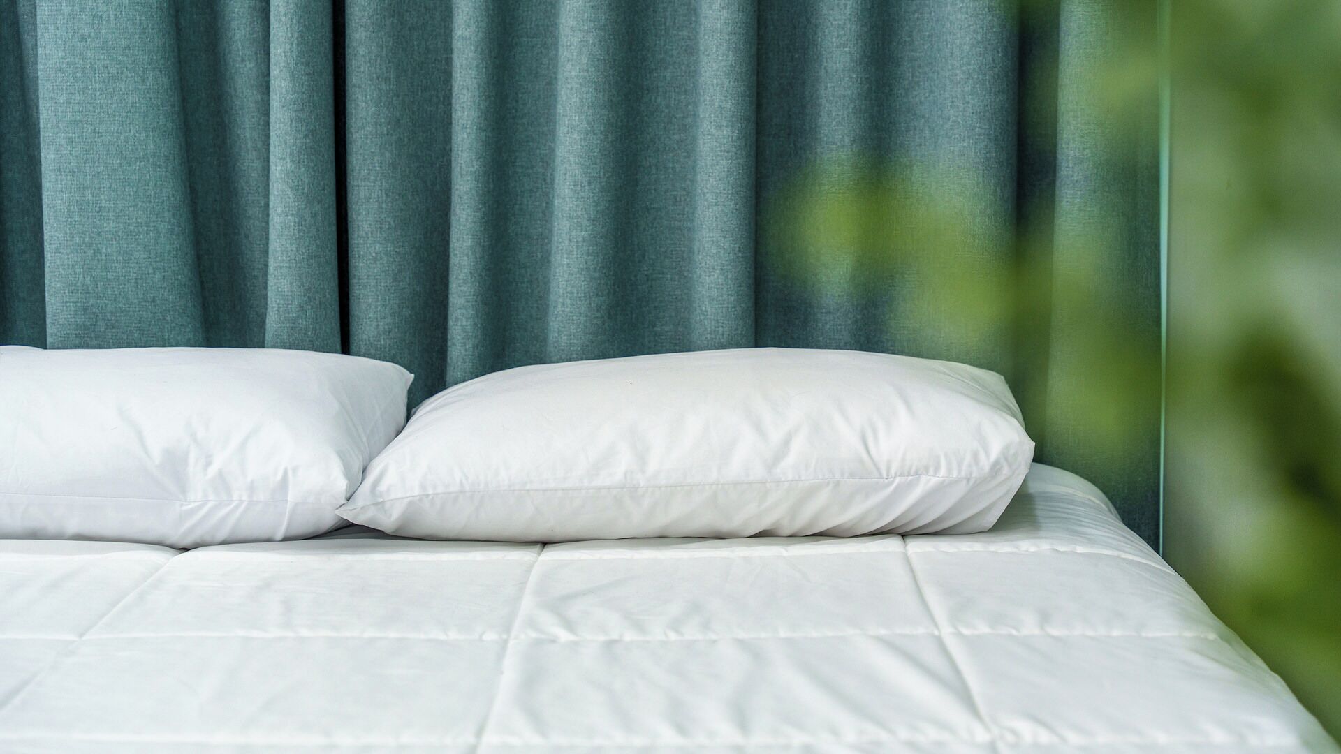 A bed with white bedding and two pillows, set against a backdrop of blue curtains.