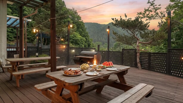 An outdoor dining area with wooden tables and benches, a grill, and string lights. - Hongcheon White Hill Pension (Hongcheon)