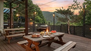 An outdoor dining area with wooden tables and benches, a grill, and string lights.