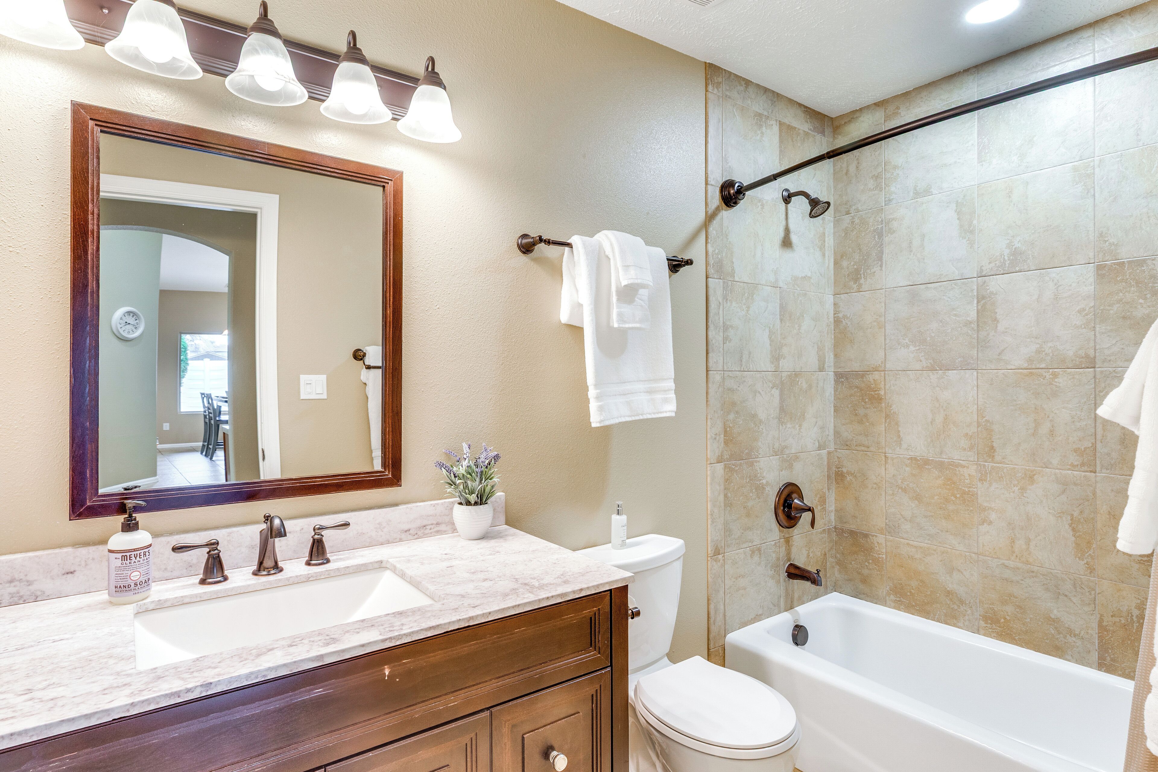 A bathroom with a double sink vanity, a toilet, and a bathtub. There is a mirror above the sink and a shower curtain rod above the bathtub.