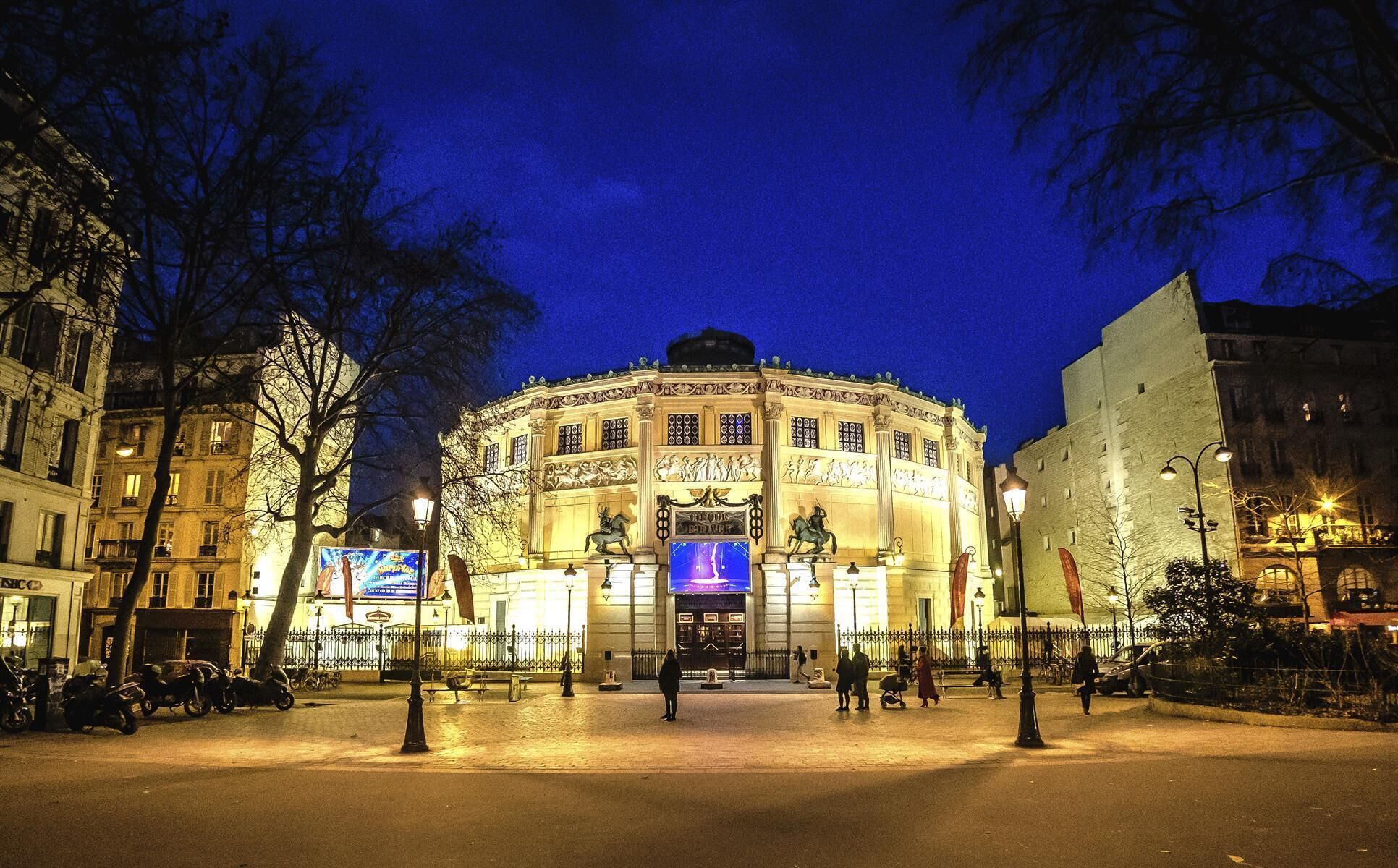 A historic building with classical architecture, a central courtyard, and a large illuminated sign.