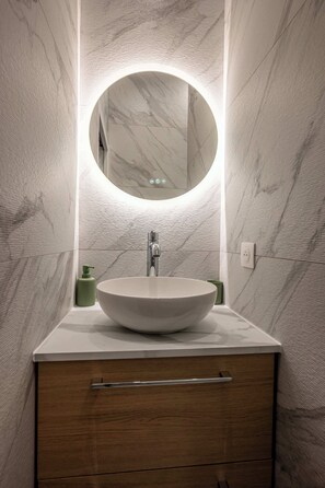 Ein modernes Badezimmer mit einem runden Spiegel, einem weißen Waschbecken und einem Holzschrank.