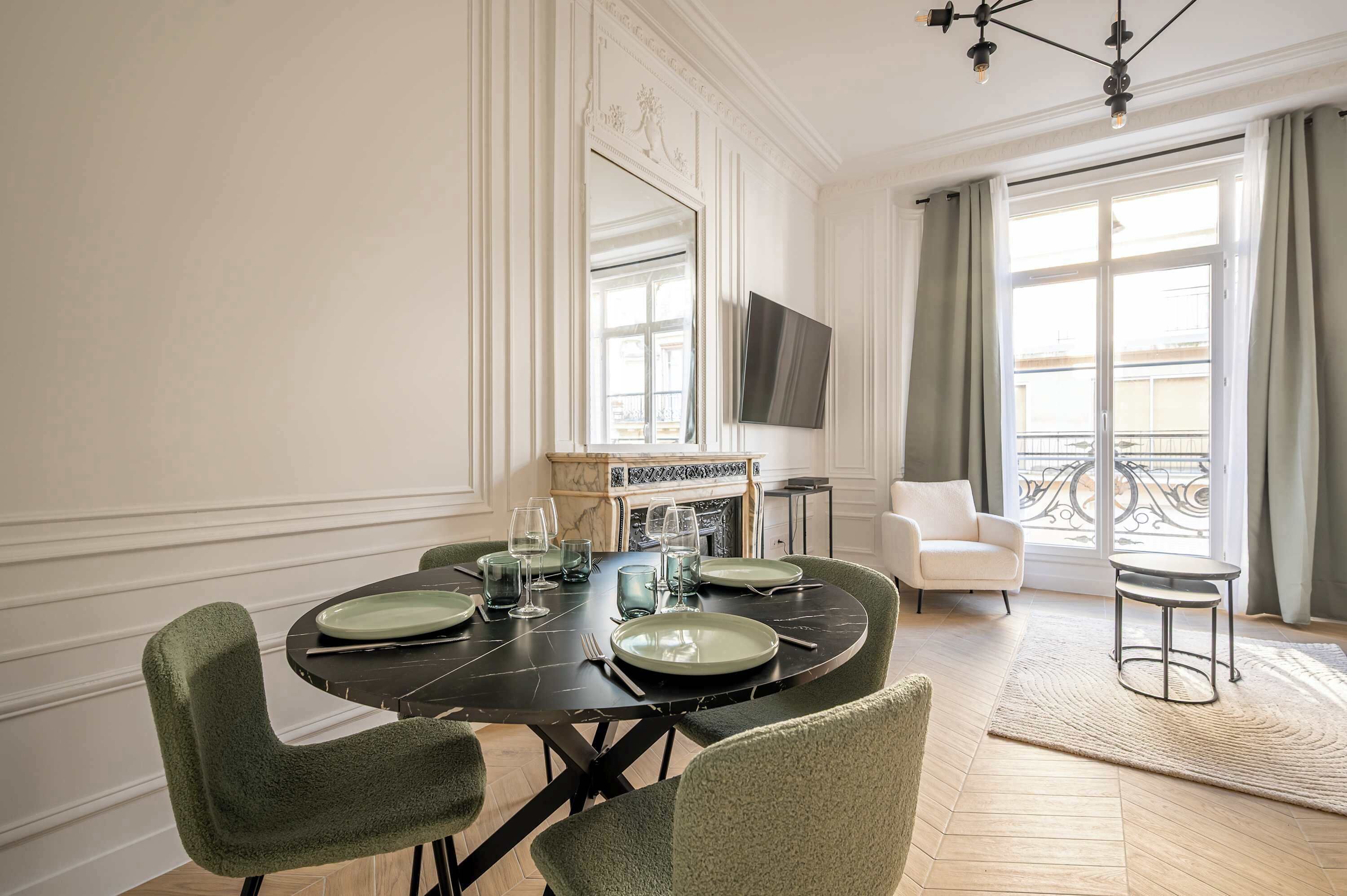 A dining room with a round table set for six, a fireplace, a television, and a balcony with a railing.