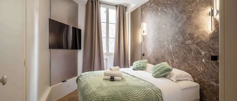 A modern bedroom with a bed, green blanket, and pillows, a TV mounted on the wall, and a stone-textured wall.