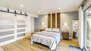 A bedroom with a bed, two bedside tables with lamps, a large window, and a sliding door. - Clarklake Lakefront Apt w/ Hot Tub & Beach (Clarklake)