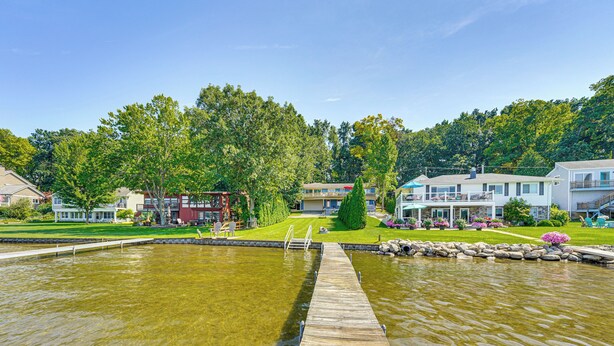 A waterfront property with a wooden dock leading into a pond, surrounded by lush greenery and residential buildings. - Clarklake Lakefront Apt w/ Hot Tub & Beach (Clarklake)