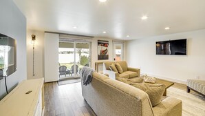 A modern living room with a sofa, armchairs, a TV, and a dining area with a table and chairs. - Clarklake Lakefront Apt w/ Hot Tub & Beach (Clarklake)
