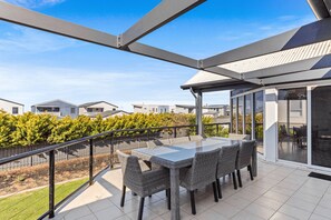 A covered outdoor patio with a table and chairs, a view of neighboring houses, and a metal railing.