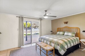 A bedroom with a bed, a ceiling fan, a bench, and a view of the outdoors through a sliding door.
