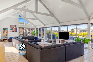 A spacious living room with a large sectional sofa, a flat-screen TV, and a bookshelf.
