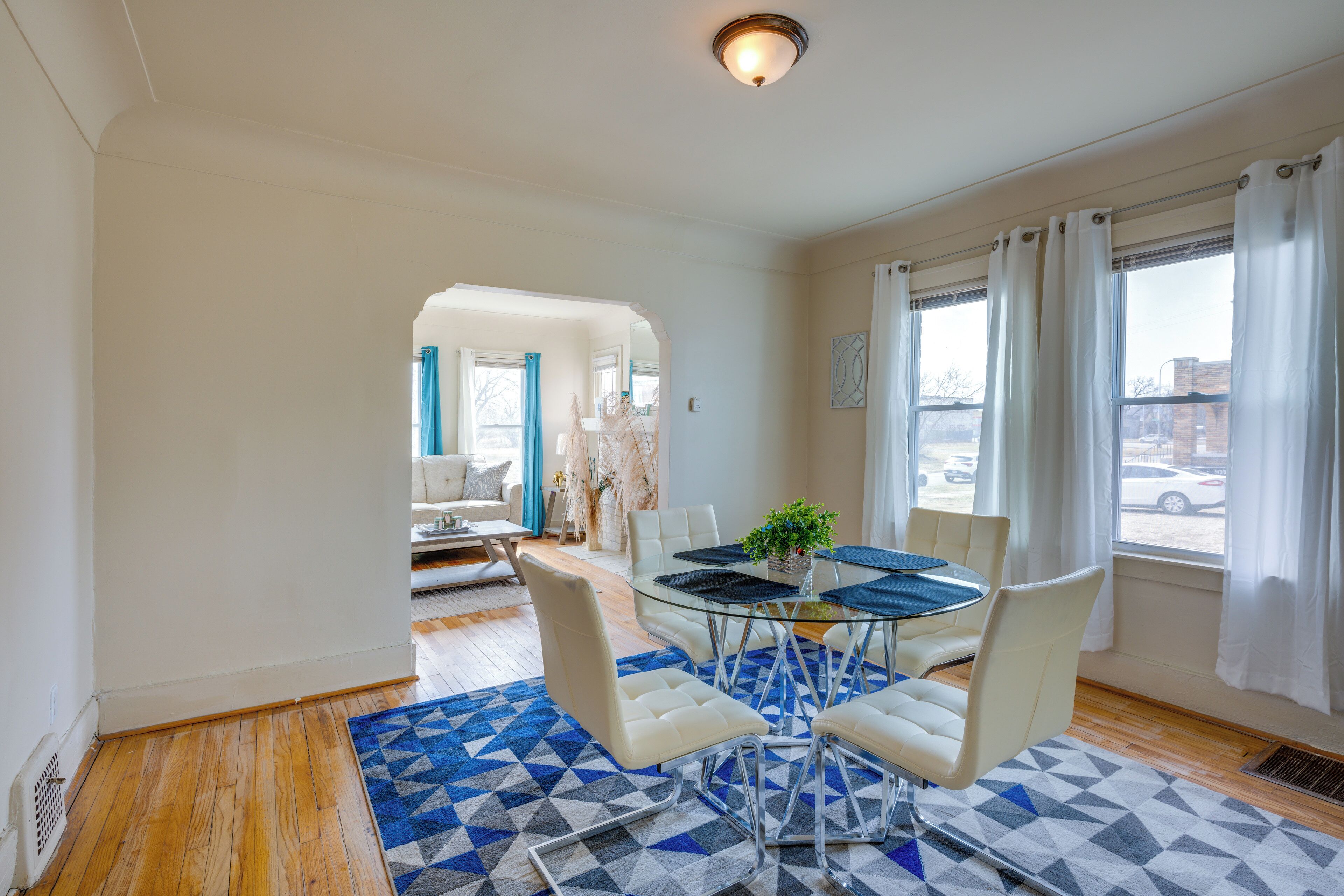 Un espace repas moderne avec une table en verre, des chaises blanches et un tapis à motifs bleus.