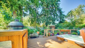 Een houten terras met een jacuzzi, een barbecue en een kleine tafel met stoelen.