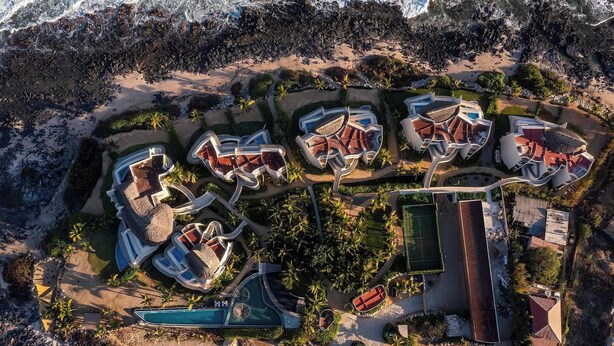 Vista aérea de un complejo turístico con varias villas, una piscina y una cancha de tenis.