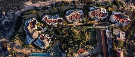 An aerial view of a resort with multiple villas, a swimming pool, and a tennis court.