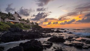 Un resort costero con costa rocosa, palmeras y vista al atardecer.