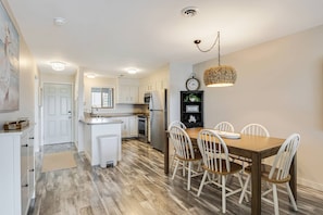 A modern kitchen with white cabinets, a wooden dining table, and a chandelier.