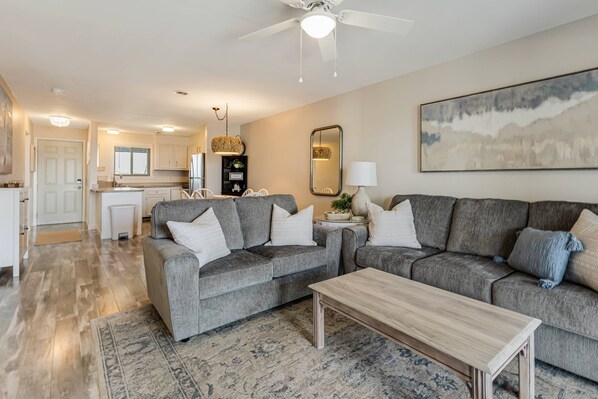 A modern living room with a grey sofa set, a wooden coffee table, and a large painting on the wall.