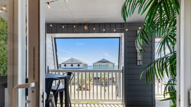 A covered outdoor area with a view of houses, a railing, and string lights. - Newly Listed Ocean View and Dog Friendly Condo on Oak Island (Oak Island)