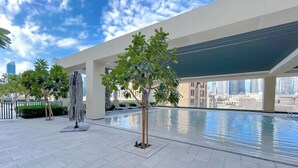 A rooftop pool area with tiled flooring, lounge chairs, umbrellas, and a view of the city skyline. - Burj Royale Elegance Cityscape From Your Balcony (Dubai)