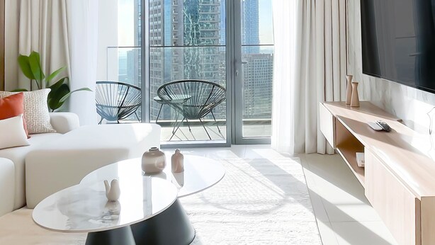 A modern living room with a large TV, a sofa, two chairs, a coffee table, and a balcony with a city view. - Burj Royale Elegance Cityscape From Your Balcony (Dubai)