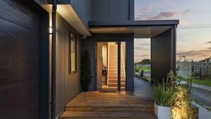 Una casa moderna con fachada de madera, una escalera de madera que lleva a una puerta y un jardín con plantas.