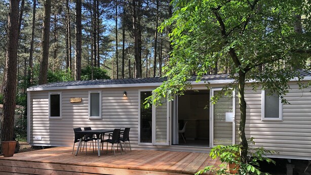 A mobile home with a deck, a table and chairs, and a small window.