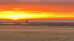 A beach scene with two people walking along the shore during sunset.