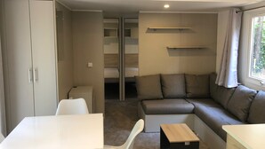 A modern, compact living space with a sofa, a small table, a white chair, and a wardrobe.