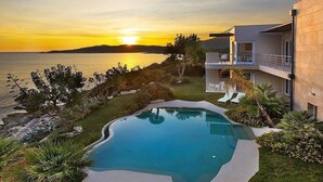 A modern house with a swimming pool, a balcony, and a view of the sea at sunset.