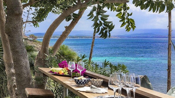 An outdoor dining area with a table set for two, overlooking a coastal view.