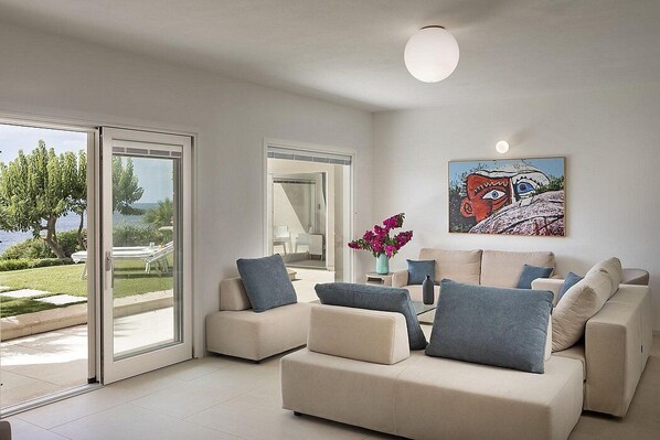 A modern living room with a sofa set, a painting, and a view of the outdoors.