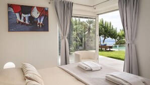 A bedroom with a bed, a massage table, and a view of a pool and garden.