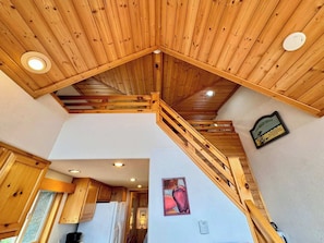 Un interior de madera con una escalera, armarios de madera, un refrigerador y un cartel en la pared.