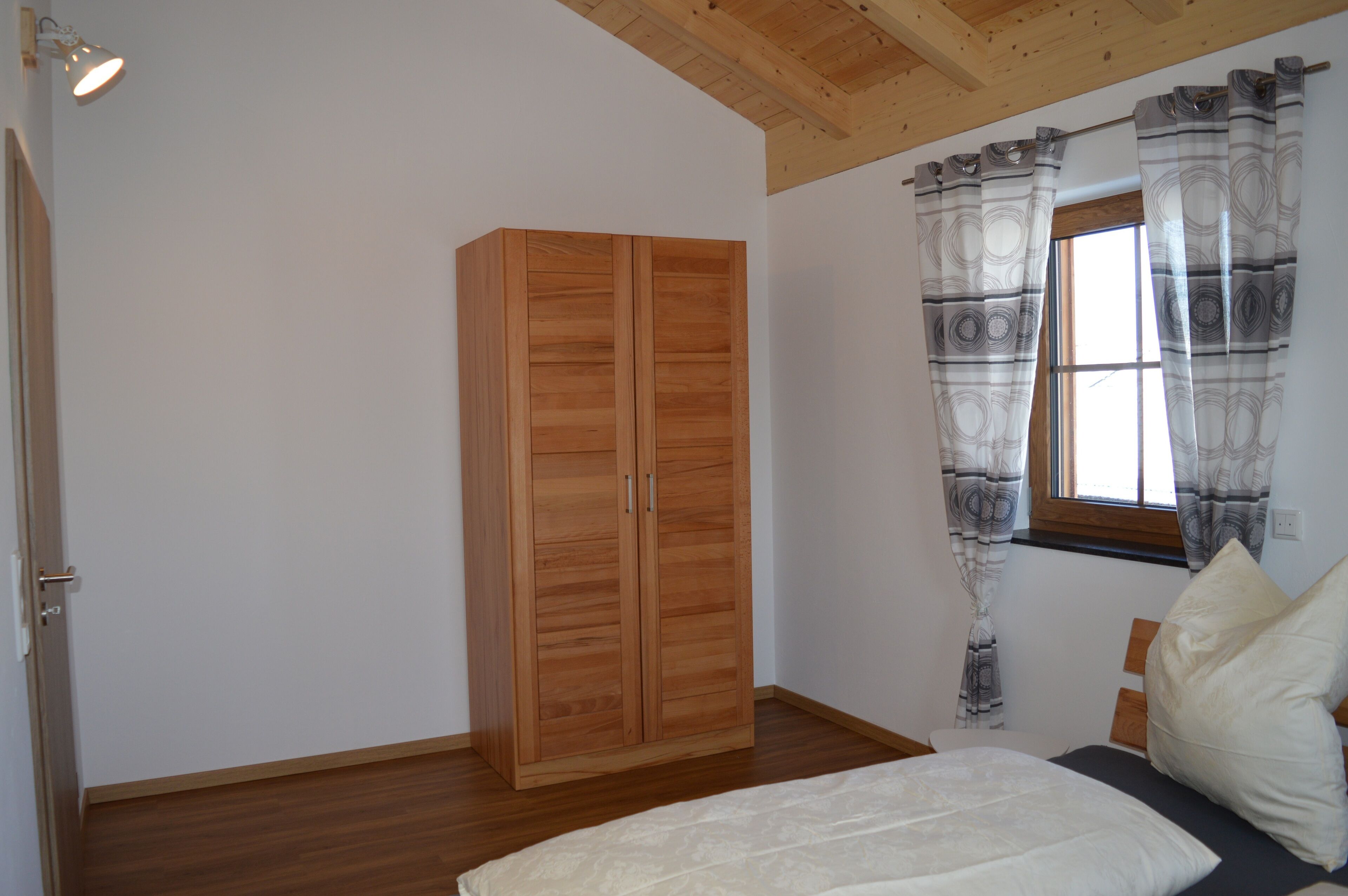 Een slaapkamer met een houten garderobe, een bed met kussens en een raam met behang gordijnen.