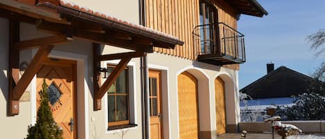 A two-story building with a wooden balcony, a covered porch, and a snow-covered landscape.