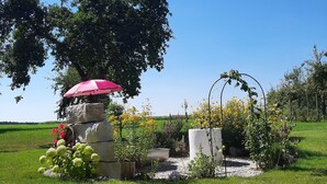Ein Garten mit einer Steinstruktur, einem roten Sonnenschirm und einem weißen Pflanzgefäß mit Blumen.