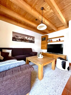 A living room with a wooden ceiling, a sofa, a coffee table, a television, and a fireplace.