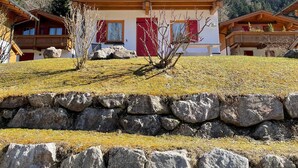 A chalet-style building with a wooden facade, multiple balconies, and a stone retaining wall in front.