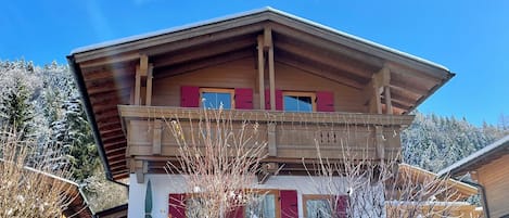 Un chalet de dos pisos con fachada de madera, un balcón y cimientos de piedra.