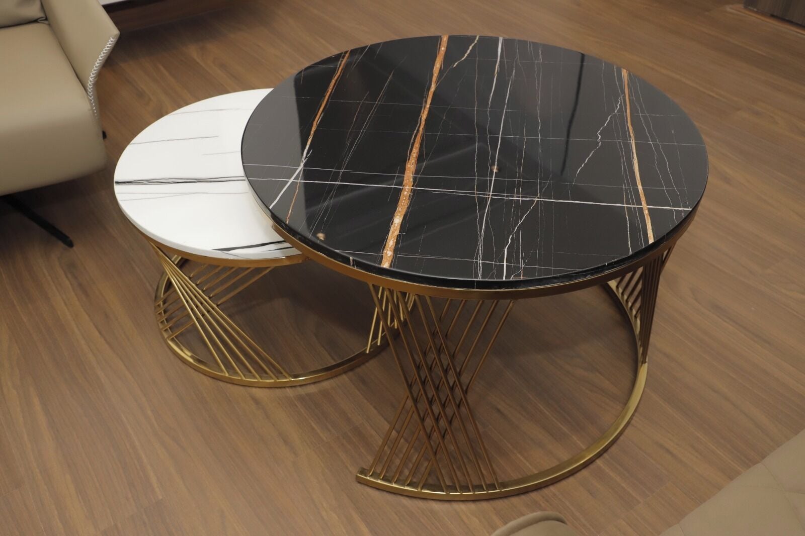 Una mesa redonda con tapa de mármol negro y patas doradas, sobre un piso de madera.