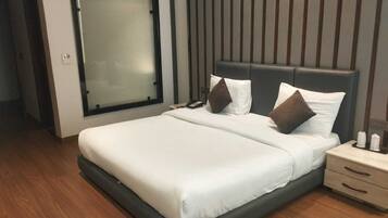 Ein modernes Hotelzimmer mit einem großen Bett, einem Nachttisch mit Telefon und Kerzen sowie einem Fenster mit Jalousien.
