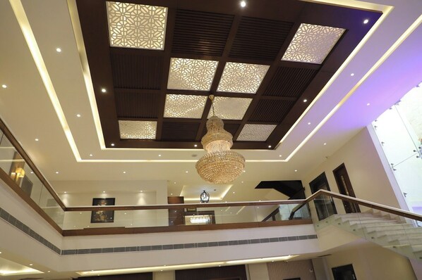 A multi-level interior with a central chandelier, patterned ceiling, and a staircase.