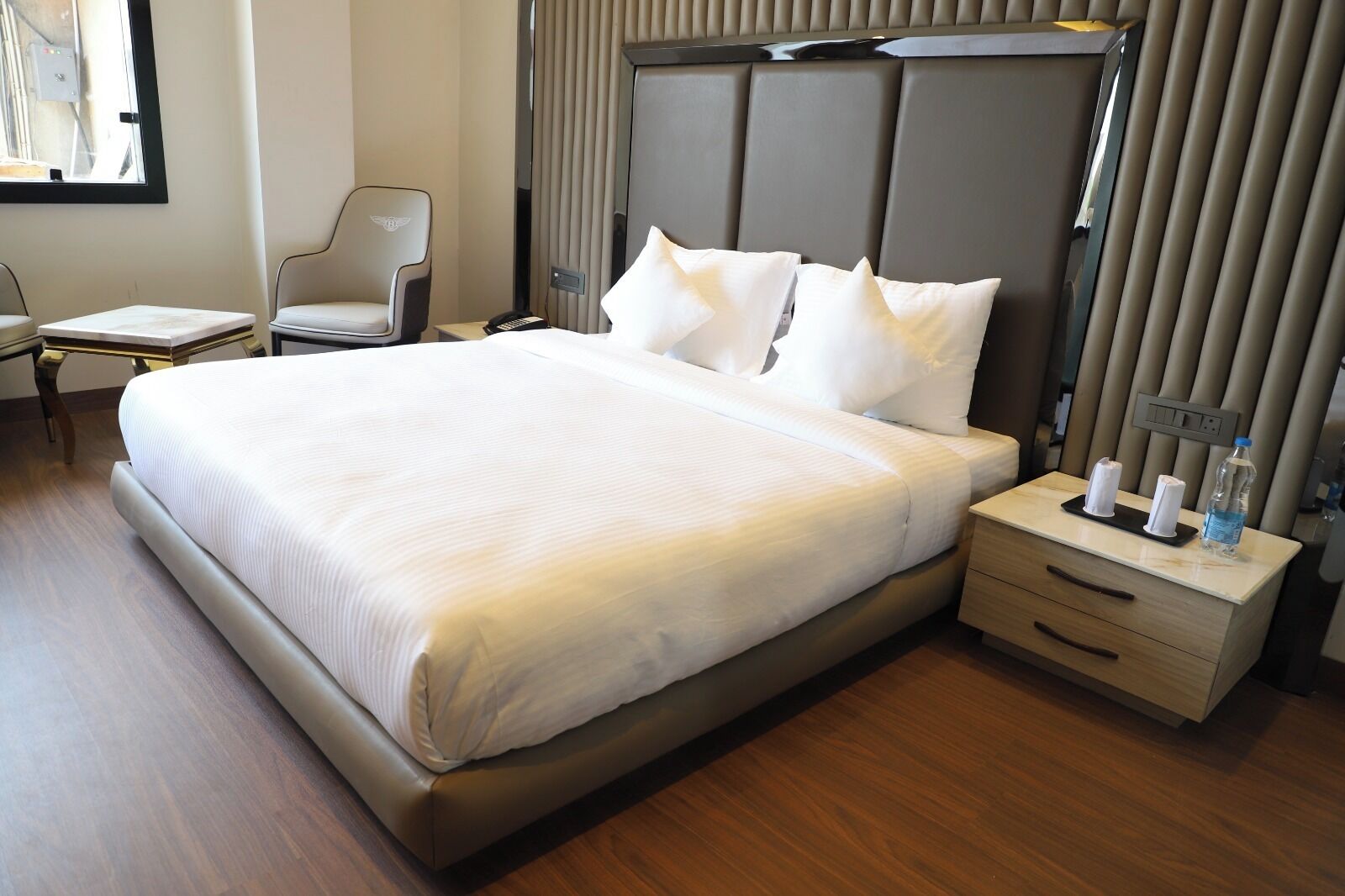 Une chambre d’hôtel avec un grand lit, une table de chevet avec une lampe, une chaise et une fenêtre.