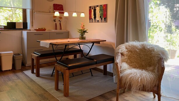 A cozy kitchen with a dining table, bench, and a fluffy chair.